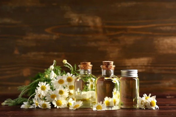 Bir şişe papatya çayı kozmetik yağı ve ahşap arka planda çiçekler.