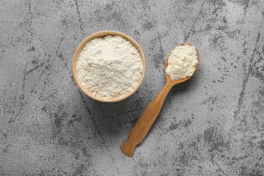 Gri arkaplanda tahta kaşıkla bir kase süt tozu.