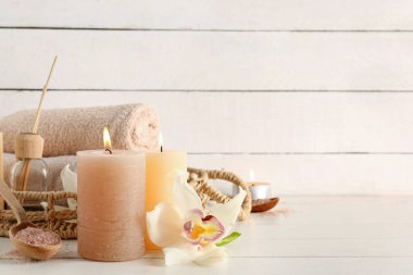 Havlular, yanan mumlar, orkide çiçekleri ve beyaz ahşap arka planda kaplıca malzemeleri olan hasır tepsi.