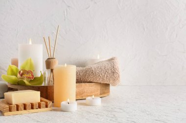 Havlulu ahşap tepsi, yanan mumlar, orkide çiçeği ve beyaz arka planda kaplıca malzemeleri.