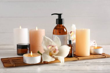 Mumları orkide çiçekleriyle yakmak ve beyaz ahşap arka planda kaplıca malzemeleri.