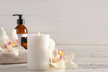 Orkide çiçekleriyle yanan mum, beyaz ahşap arka planda havlu ve spa malzemeleri.