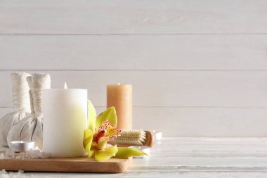 Orkide çiçeğiyle mum yakmak, beyaz ahşap arka planda deniz tuzu ve spa malzemeleri.