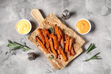 Lezzetli pişmiş tatlı patatesli ahşap tahta, biberiye ve gri grunge arka planda bir kase sos.