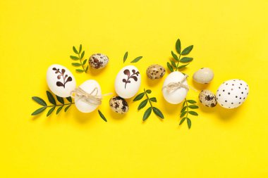 Sarı arka planda yeşil yapraklı Paskalya yumurtaları