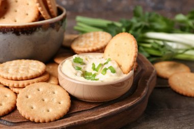 Lezzetli krakerler, bir kase sos ve yeşil soğan, ahşap masada, arka planda grunge karşı, yakın plan.