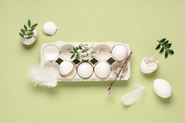 Cardboard holder with Easter eggs, feathers, leaves, pussy willow branches and gypsophila flowers on green background