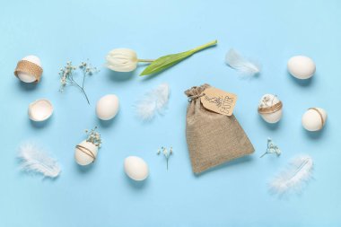 Mavi arka planda çiçek, tüy ve çuval bezi olan Paskalya yumurtaları