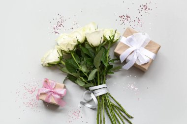 Gri arka planda hediye kutuları olan beyaz gül çiçekleri.