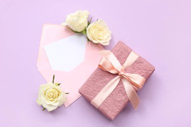 Güzel beyaz gül çiçekleri hediye kutusu, zarf ve mor arka planda boş kağıt kart.