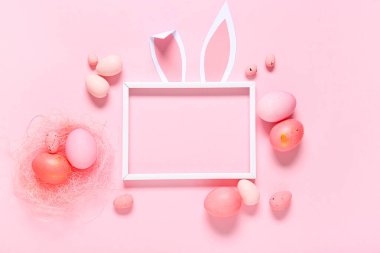 Kağıt tavşan kulaklı fotoğraf çerçevesi ve pembe arka planda Paskalya yumurtaları.