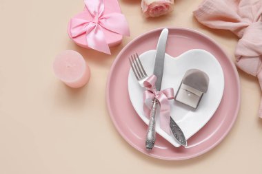 Nişan yüzüğüyle, mumla, hediye kutusuyla ve bej arka planda gül çiçeğiyle güzel bir masa.