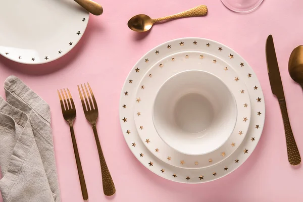 Pembe arka planda altın çatal bıçak takımı olan güzel bir masa.