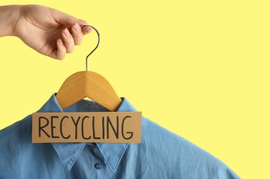 Sarı arka planda asılı tişört ve RECYCLING işareti olan bir kadın.