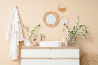 Çiçek açan dalları olan vazolar, lavabo ve banyo malzemeleri odada bej duvarın yanında.