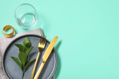 Altın çatal bıçak takımı ve turkuaz arka planda taze yapraklarla güzel bir masa.
