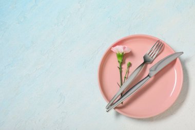 Gümüş çatal bıçak takımı ve açık mavi arka planda karanfil çiçeği olan güzel bir masa.
