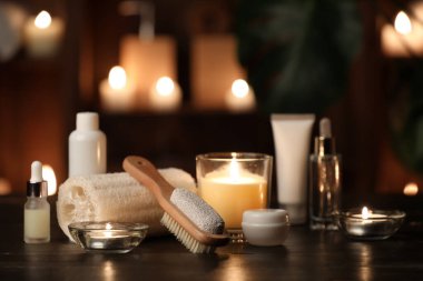 Kozmetik ürünleri şişeleri, lif süngeri ve karanlık odadaki ahşap masada yanan mumlar.