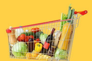 Sarı arka planda farklı taze ürünleri olan alışveriş arabası.