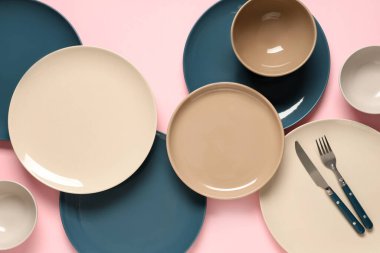 Pembe arka planda gümüş çatal bıçaklı farklı temiz tabaklar.