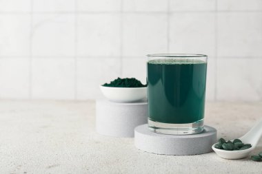 Bir bardak taze spirulina iç ve bej grunge masasında haplarla kepçele, yakın plan.