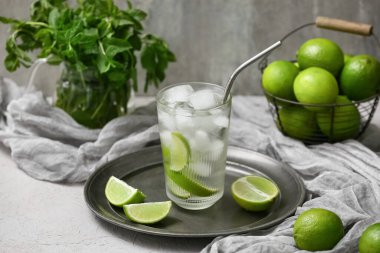 Bir bardak kireç suyu ve nane şekeri gri arka planda beyaz masada.