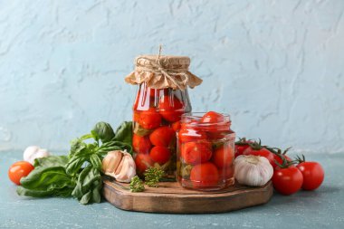 Fesleğenli konserve domates kavanozları ve turkuaz arkaplanda sarımsak.