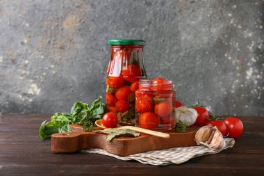 Kavanozlar dolusu fesleğenli, defne yapraklı ve ahşap masada gri grunge arka planda sarımsaklı domates.