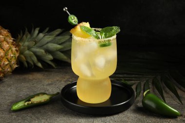 Jalapeno biberli bir bardak margarita kokteyli ve gri grunge masasında koyu arka planda ananas.