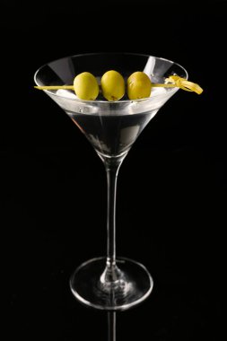 Siyah arka planda zeytinli bir bardak taze martini.