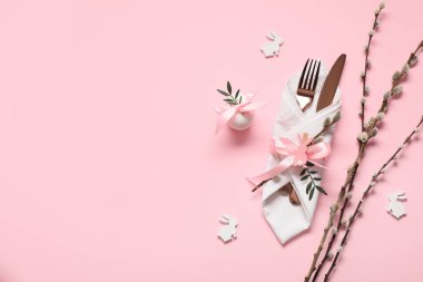 Easter table setting with pussy willow branches, egg, decorative bunnies and olive branches on pink background