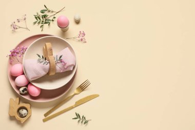 Paskalya sofrasında boyalı yumurtalar, çingene çiçekleri ve bej arka planda zeytin dalları.