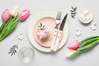 Paskalya sofrasında yumurta, lale çiçeği ve gri arka planda zeytin dalları var.