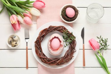 Paskalya sofrasında yumurta, çelenk, zeytin dalları ve beyaz ahşap arka planda lale çiçekleri.