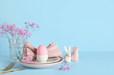 Boyanmış yumurta, çingene çiçekleri ve mavi arka planda seramik tavşanlarla Paskalya sofrası.