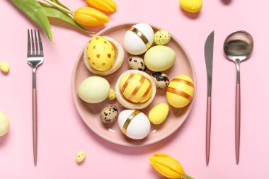 Paskalya yumurtaları, lale çiçekleri ve pembe arka planda çatal bıçak takımı.