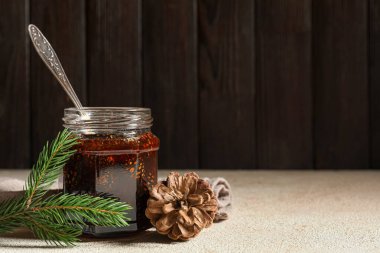 Kavanoz dolusu lezzetli kozalak reçeli, kaşık ve köknar ağacı dalı, ahşap arka planda.
