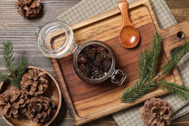 Ahşap arka planda bir kavanoz lezzetli çam kozalağı reçeli, kaşık ve köknar ağacı dalları olan tahta pano.