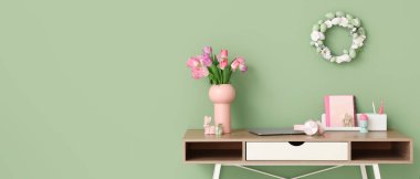 Laptoplu çalışma alanı, lale çiçekleri ve yeşil duvarın yanındaki Paskalya süslemeleri. Tasarım için pankart