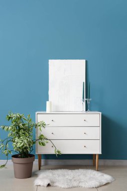 Tuvalli dolap, saksı ve mavi duvarın yanındaki mumlar.