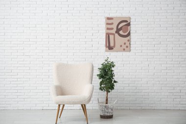 Koltuk, çiçek ve resim beyaz tuğla duvarda.