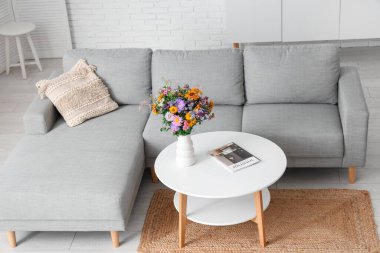 Oturma odasının iç tarafındaki sehpada yabani çiçekler olan rahat bir kanepe ve vazo.