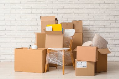 Beyaz tuğla duvarın yanında paketlenmiş sandalye ve karton kutular. Taşınma konsepti