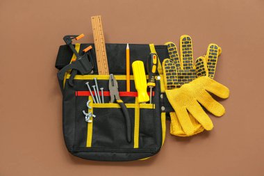 Kahverengi arka planda marangoz aletleri ve eldivenleri olan alet kemeri.