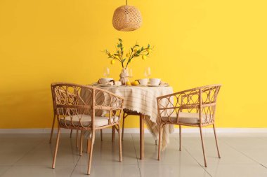 Yemek odasının içi, masa düzeniyle ve sarı duvarın yanında güzel limon ağacı dallarıyla dolu.