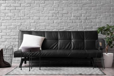 Oturma odasının içinde siyah kanepe, puf ve bitki