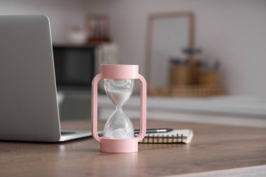 Kum saati, modern dizüstü bilgisayar ve defter odadaki masada.