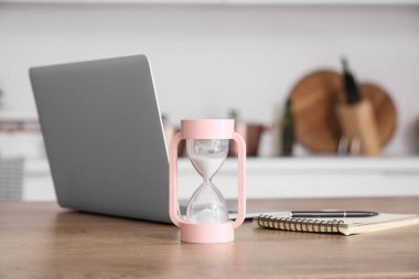 Kum saati, modern dizüstü bilgisayar ve defter odadaki masada.