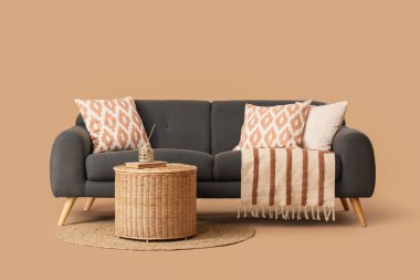 Kahverengi arka planda yastıklı, battaniyeli ve hasır sepetli rahat siyah kanepe.