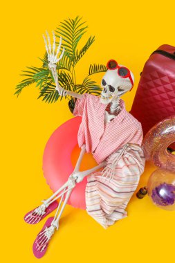 Kumsal aksesuarları ve sarı arka planda bavulu olan insan iskeleti.